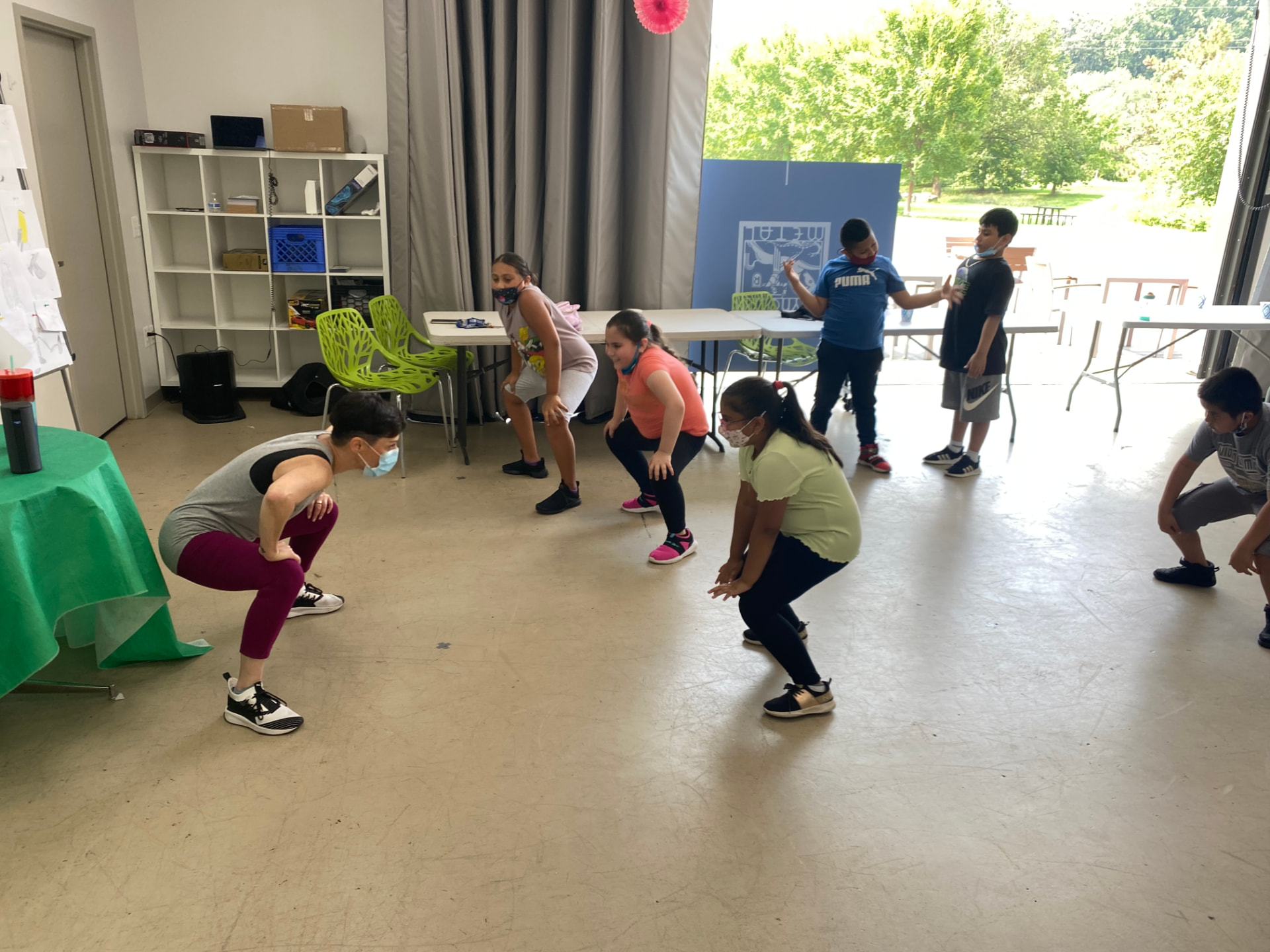 Children and a teaching artist wearing masks practice dance movements together in a community room.