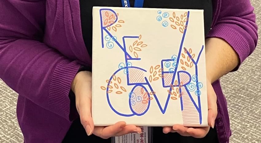 A small canvas painted with the word 'Recovery' in stylized blue and orange lettering.