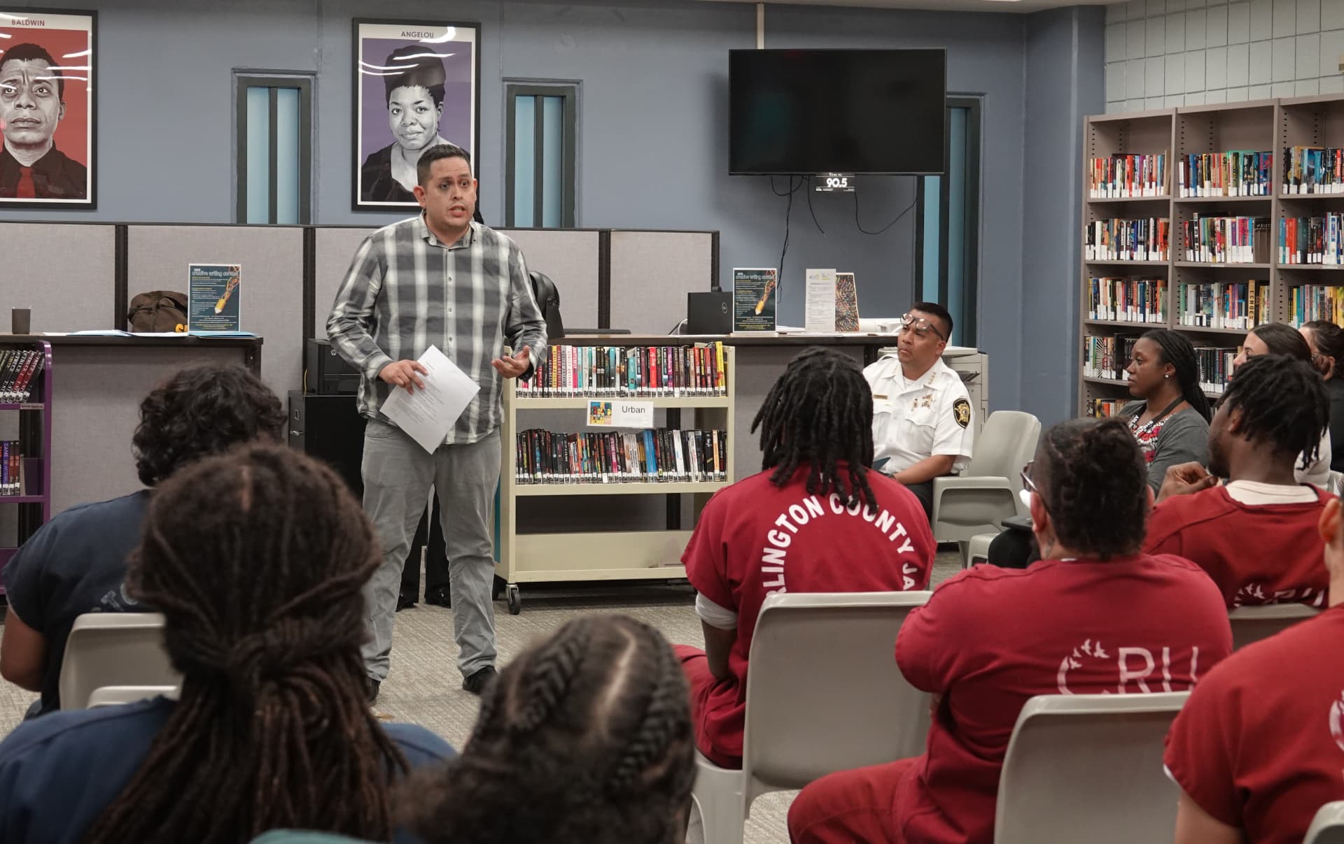 A teaching artist addresses a seated audience of participants during a creative writing contest reading.