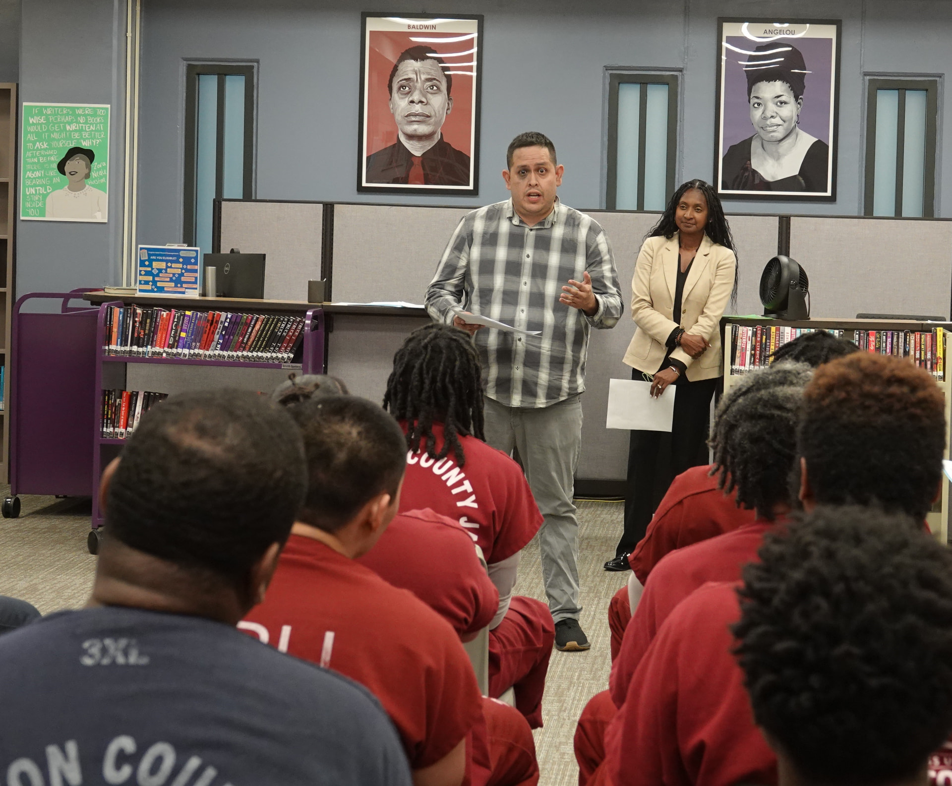 A teaching artist speaks to a seated group of participants at a creative writing contest inside a facility library.