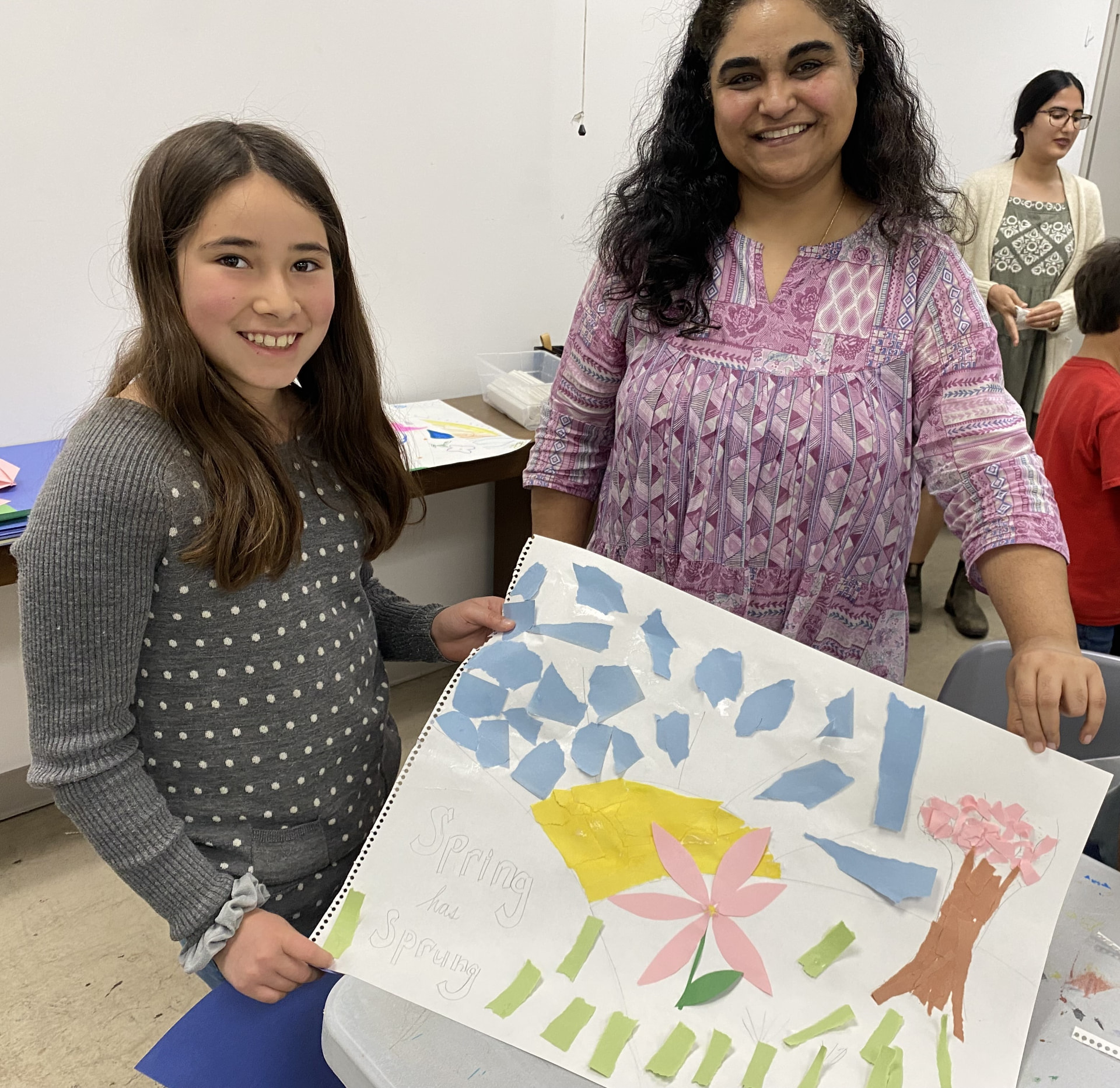 A young participant and a teaching artist hold up a torn-paper collage reading 'Spring has Sprung'.