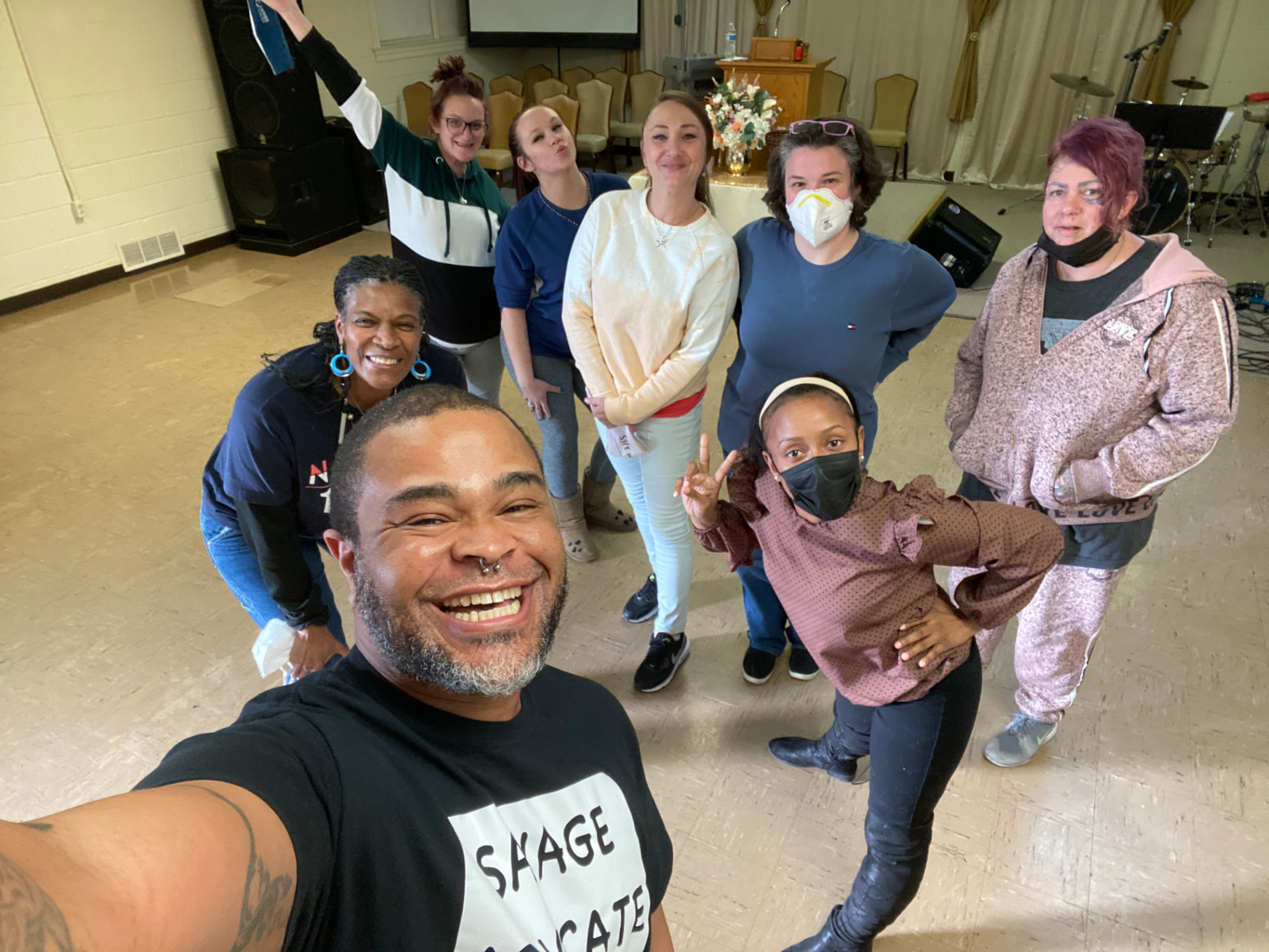 Participants and teaching artists pose together for a group photo in a community hall.
