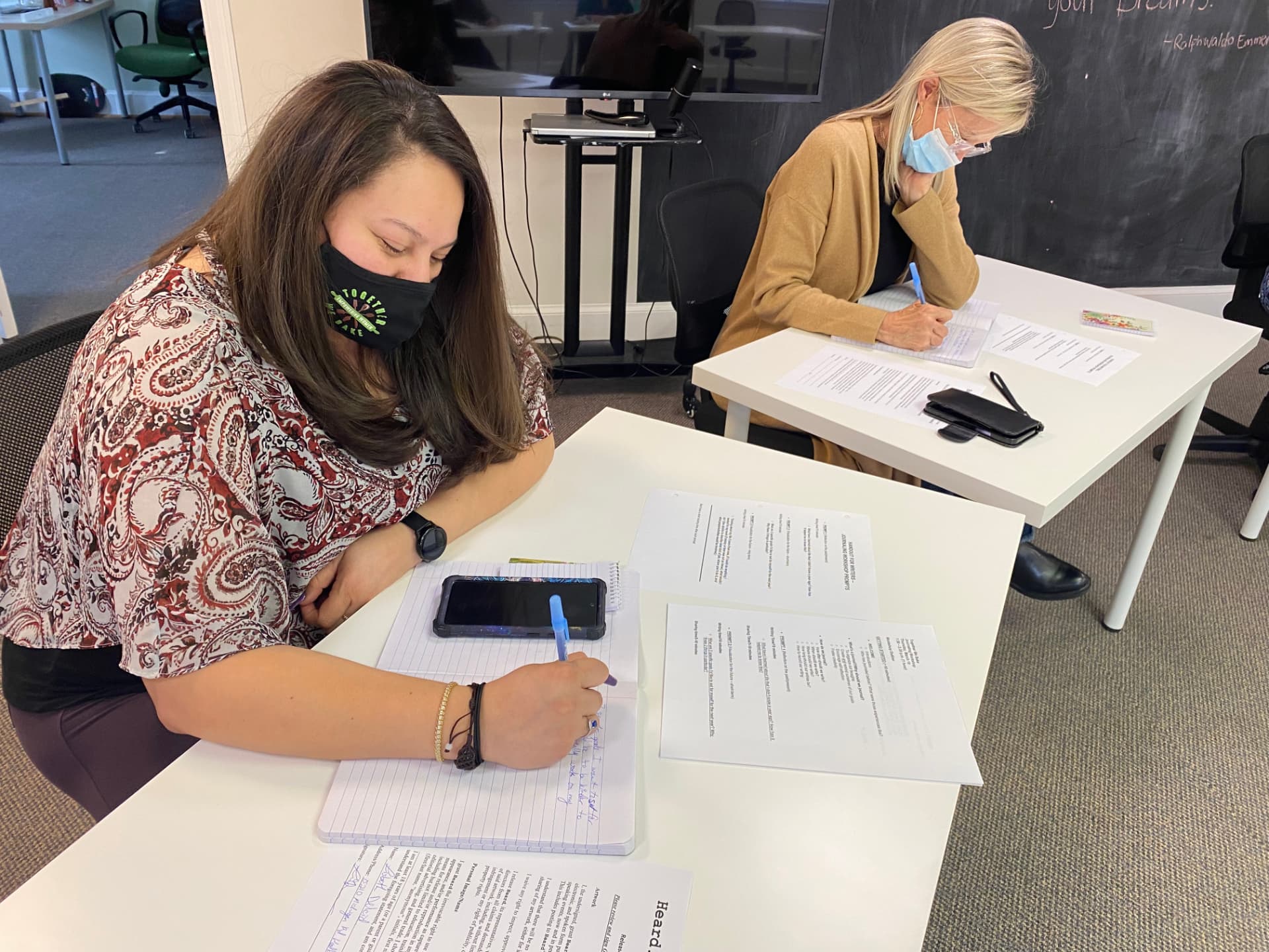 Two participants write in notebooks at separate tables during a journaling workshop.