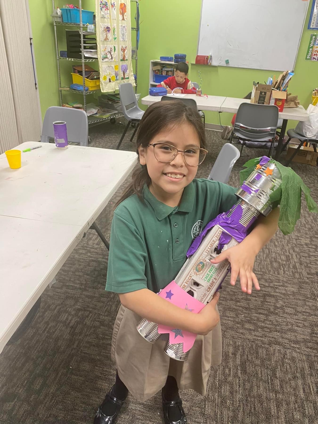 A student holds a sculpture she built from an egg carton and tin cans in a recycled-materials art class.
