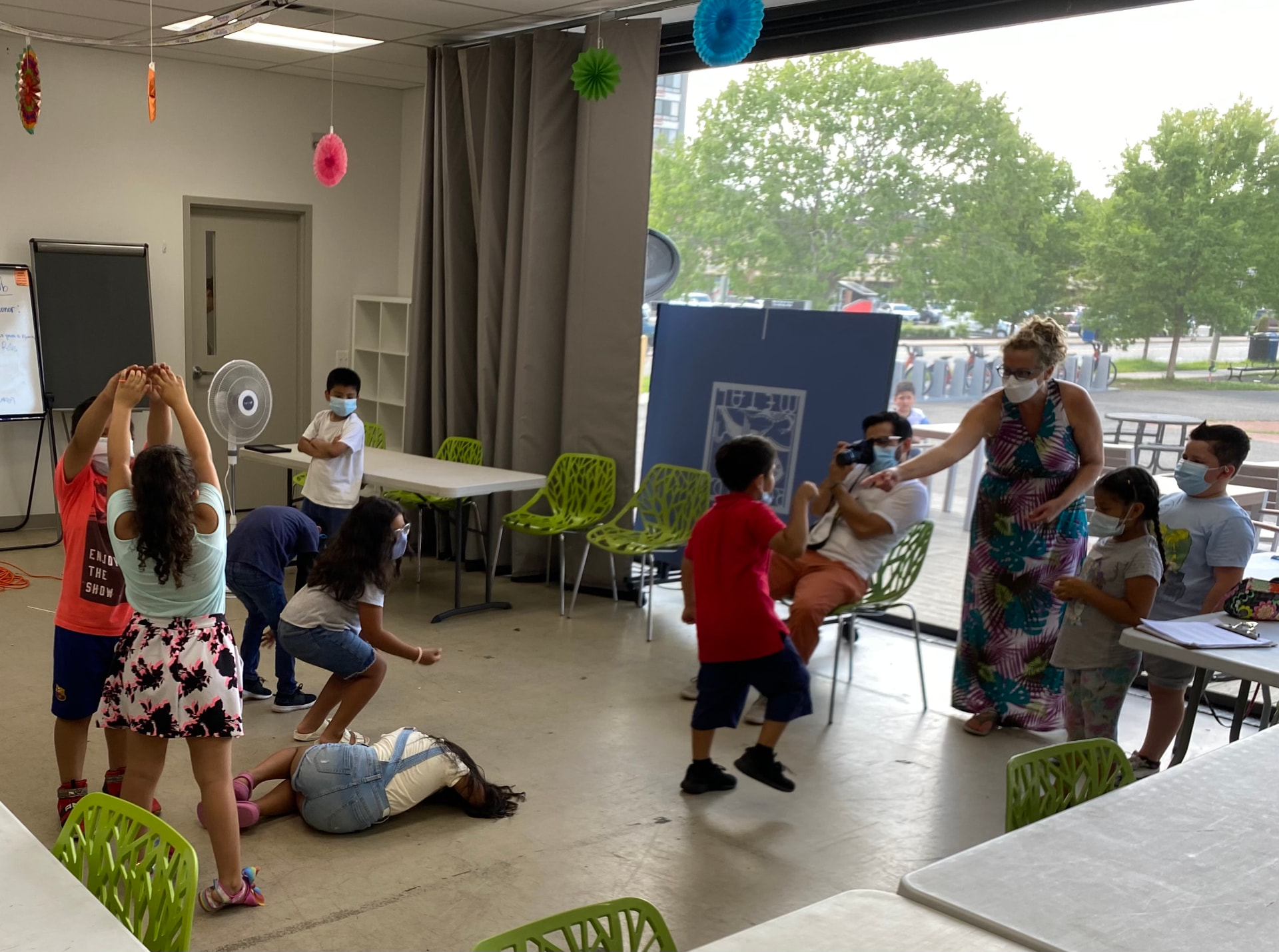 Children and adults take part in an improvisation exercise in a community program space.